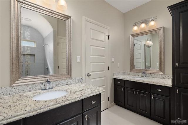 full bathroom with two vanities, tiled shower, and a sink