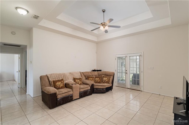 tiled living room with ceiling fan, a raised ceiling, a high ceiling, and french doors