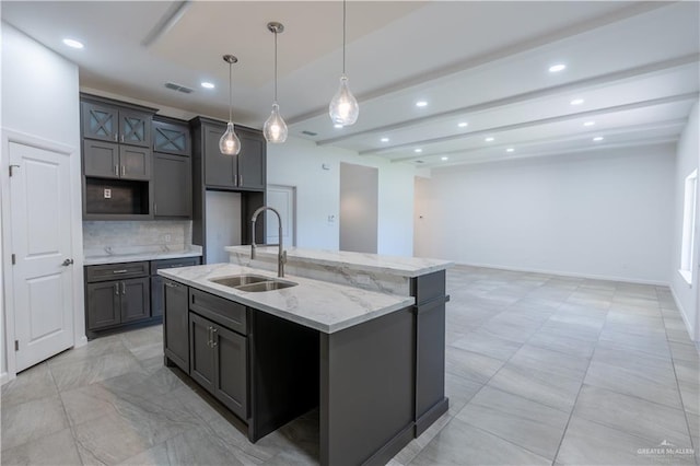 kitchen with tasteful backsplash, sink, an island with sink, and decorative light fixtures