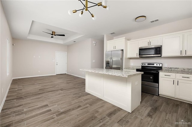 kitchen with a kitchen island, appliances with stainless steel finishes, light stone counters, a tray ceiling, and white cabinetry