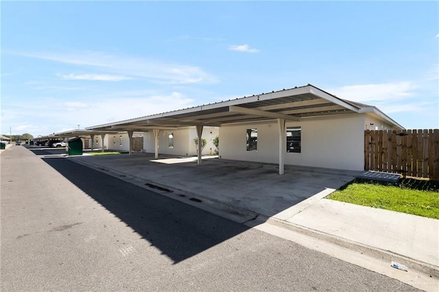 ranch-style house featuring covered parking, fence, and stucco siding