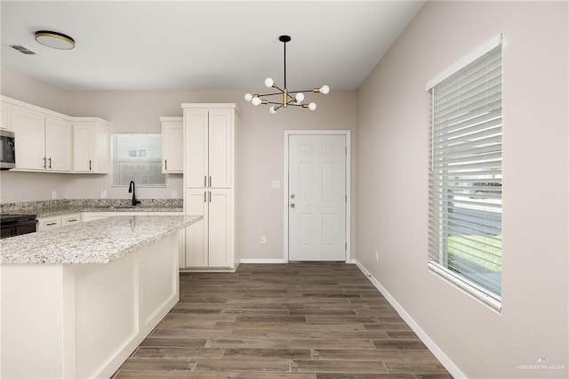 kitchen with a sink, white cabinetry, a center island, stainless steel microwave, and decorative light fixtures