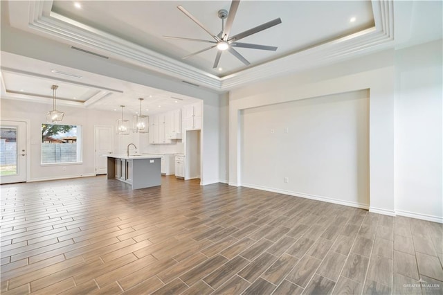 unfurnished living room featuring visible vents, dark wood finished floors, a ceiling fan, a raised ceiling, and a sink