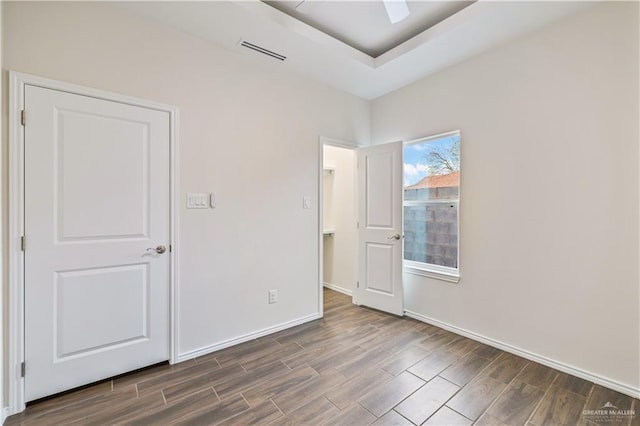 unfurnished bedroom featuring ceiling fan, wood finish floors, visible vents, baseboards, and a tray ceiling