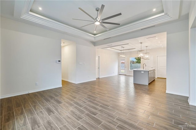 unfurnished living room with ceiling fan with notable chandelier, dark wood-type flooring, a sink, visible vents, and a raised ceiling