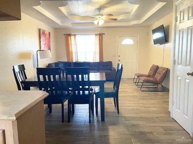 dining space with ceiling fan, wood-type flooring, and a raised ceiling