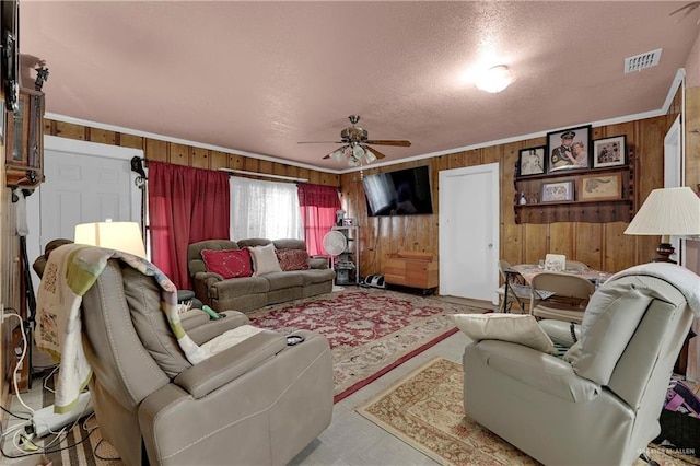 living room with wooden walls, crown molding, ceiling fan, and a textured ceiling