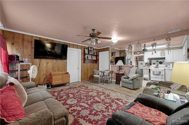 living room with ceiling fan, wood walls, and ornamental molding