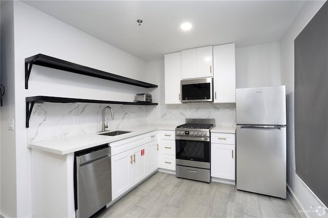 kitchen with white cabinets, appliances with stainless steel finishes, tasteful backsplash, sink, and light hardwood / wood-style flooring