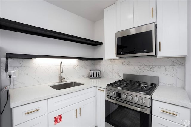 kitchen featuring appliances with stainless steel finishes, white cabinetry, sink, backsplash, and light stone counters