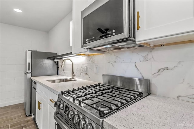 kitchen featuring light stone countertops, white cabinets, stainless steel appliances, decorative backsplash, and sink