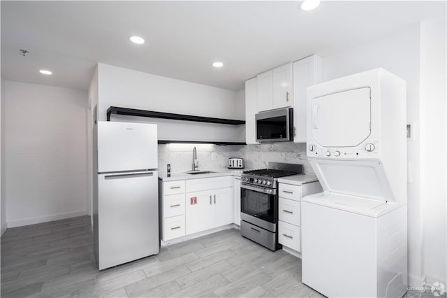 kitchen featuring white cabinets, stacked washer / drying machine, stainless steel appliances, sink, and light hardwood / wood-style flooring