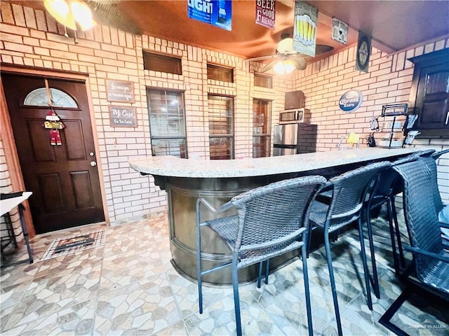 bar featuring indoor bar, brick wall, stainless steel microwave, and ceiling fan