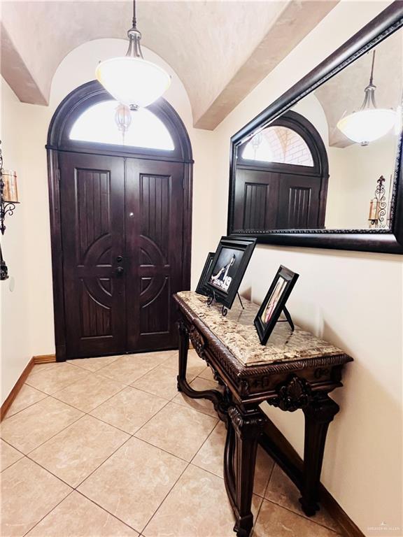 foyer with lofted ceiling, baseboards, and light tile patterned flooring