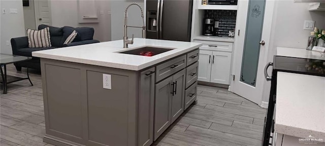 kitchen with sink, stainless steel fridge, gray cabinetry, stove, and a center island with sink