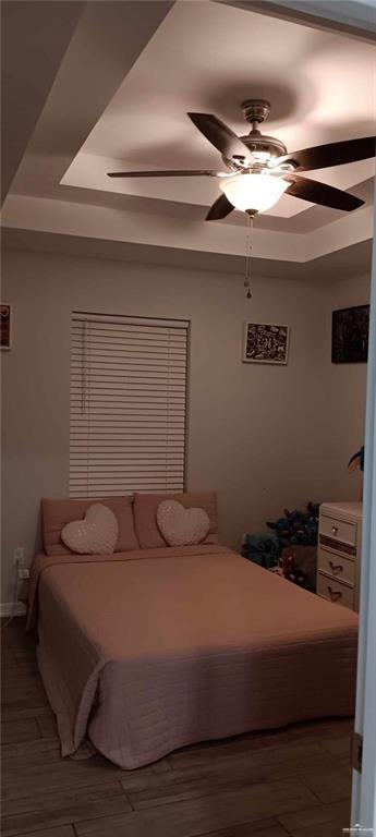 bedroom with a raised ceiling, dark hardwood / wood-style flooring, and ceiling fan