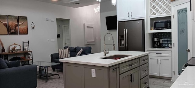 kitchen featuring sink, stainless steel fridge with ice dispenser, light wood-type flooring, gray cabinets, and an island with sink