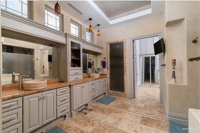 bathroom with a tray ceiling, double vanity, visible vents, a high ceiling, and a sink