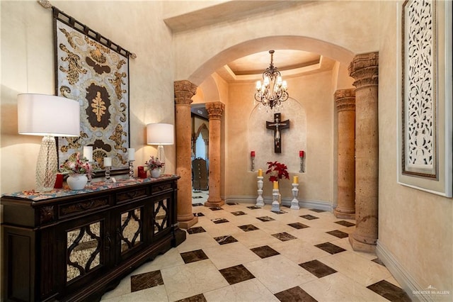 corridor with a tray ceiling, decorative columns, arched walkways, and baseboards