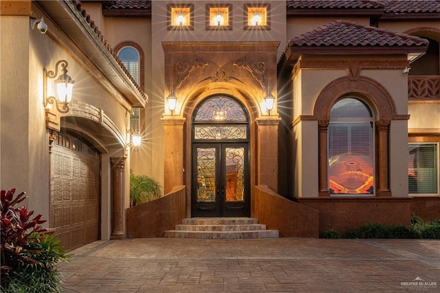 entrance to property with stucco siding, a tiled roof, decorative driveway, and french doors