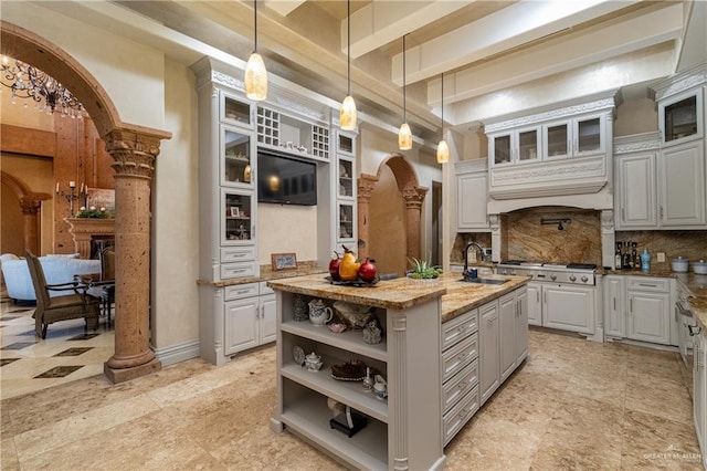 kitchen with tasteful backsplash, a center island with sink, arched walkways, pendant lighting, and open shelves