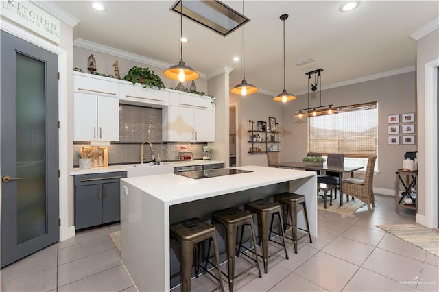 kitchen featuring pendant lighting, a breakfast bar area, light countertops, white cabinets, and a sink