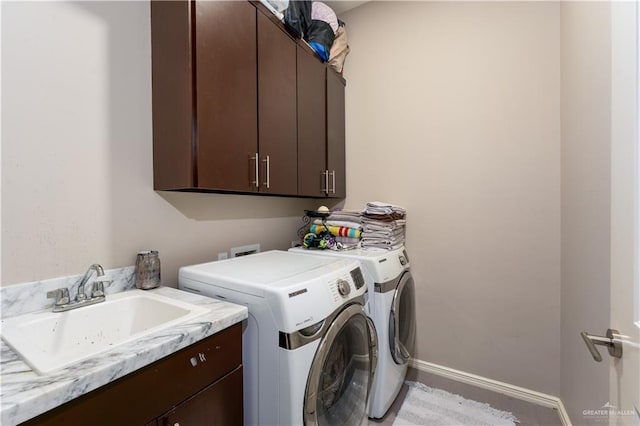 washroom with cabinet space, baseboards, a sink, and washing machine and clothes dryer