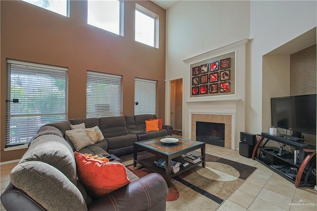 living room featuring a tile fireplace, light tile patterned floors, a healthy amount of sunlight, and a high ceiling