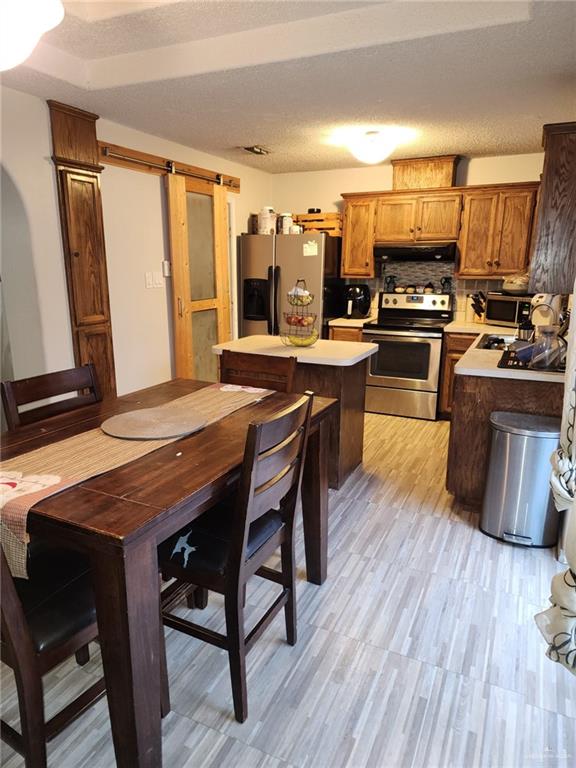 kitchen featuring a textured ceiling, light wood-type flooring, stainless steel appliances, a barn door, and decorative backsplash