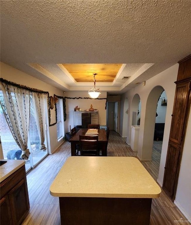 kitchen with pendant lighting, a center island, a tray ceiling, wood-type flooring, and a textured ceiling