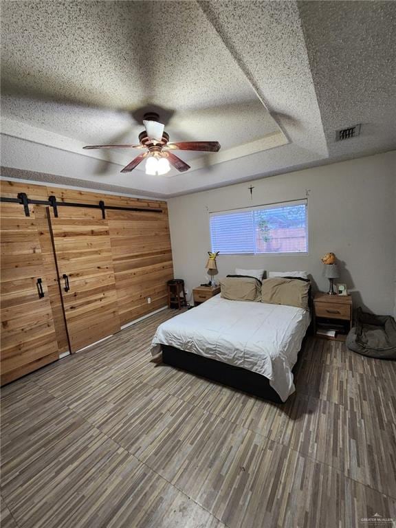 bedroom featuring ceiling fan, hardwood / wood-style floors, a textured ceiling, and a tray ceiling