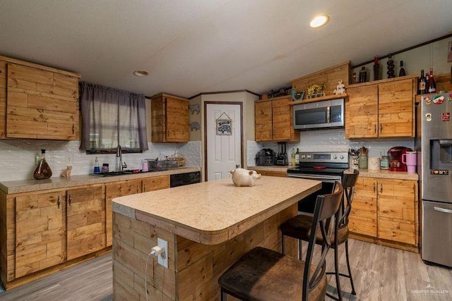 kitchen with a kitchen bar, appliances with stainless steel finishes, tasteful backsplash, sink, and light hardwood / wood-style floors