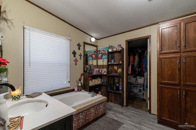 bathroom featuring a textured ceiling, vanity, vaulted ceiling, tiled tub, and hardwood / wood-style flooring