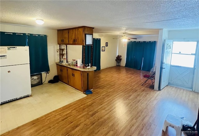 593 5th St, Raymondville, TX 78580 - kitchen with freestanding refrigerator, a textured ceiling, brown cabinets, light wood finished floors, and ceiling fan