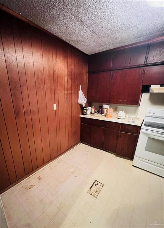 593 5th St, Raymondville, TX 78580 - kitchen featuring white electric stove, a textured ceiling, light countertops, wood walls, and under cabinet range hood
