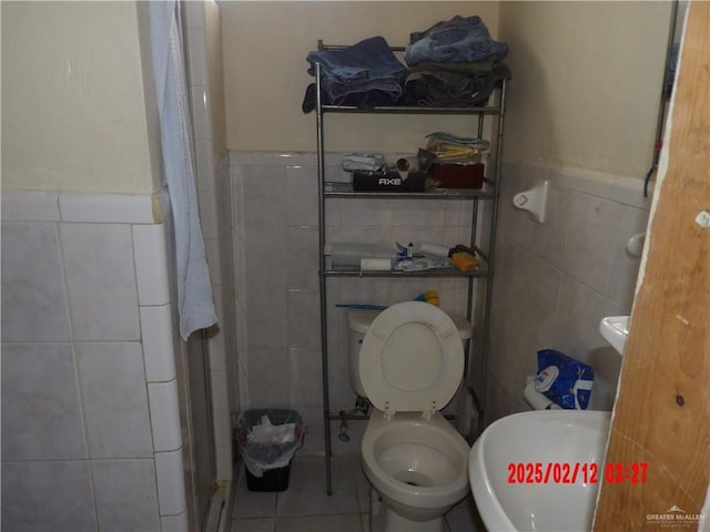 bathroom with toilet, tile patterned flooring, a shower with door, and tile walls