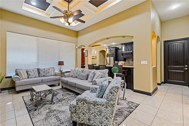 living room with light tile patterned flooring, a towering ceiling, coffered ceiling, and ceiling fan