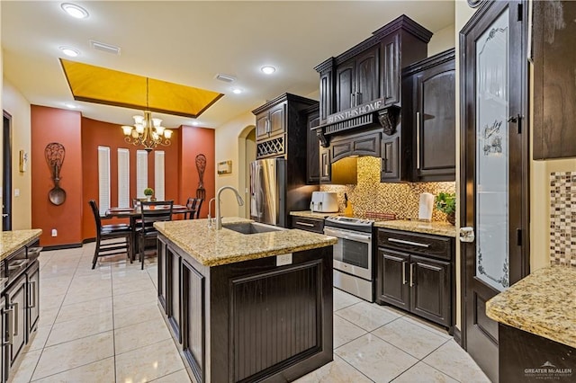 kitchen with a raised ceiling, backsplash, hanging light fixtures, stainless steel appliances, and a center island with sink