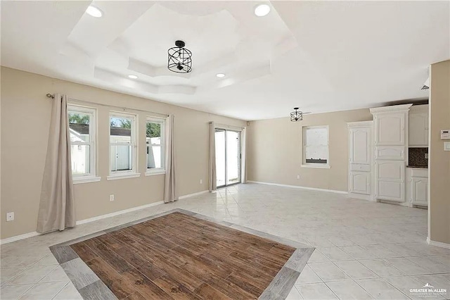 unfurnished living room with light tile patterned floors, a tray ceiling, recessed lighting, and baseboards