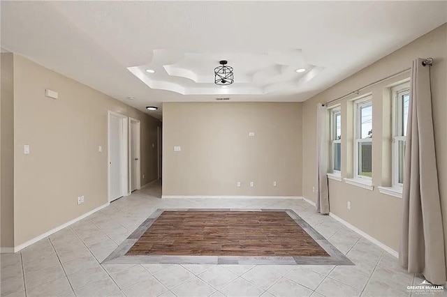 unfurnished room with a tray ceiling, baseboards, and light tile patterned floors