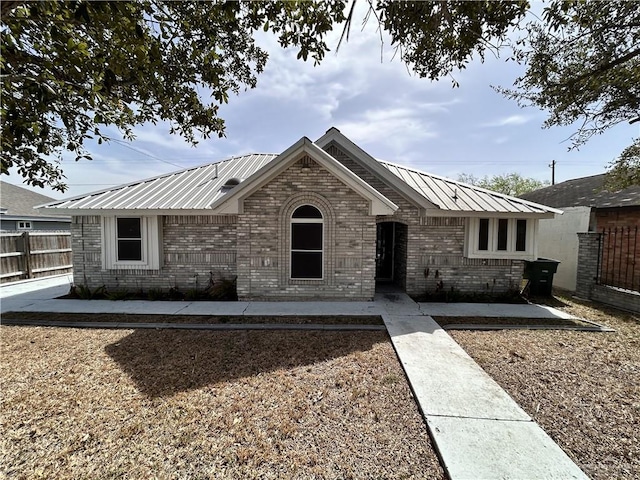 ranch-style home featuring fence, metal roof, and brick siding