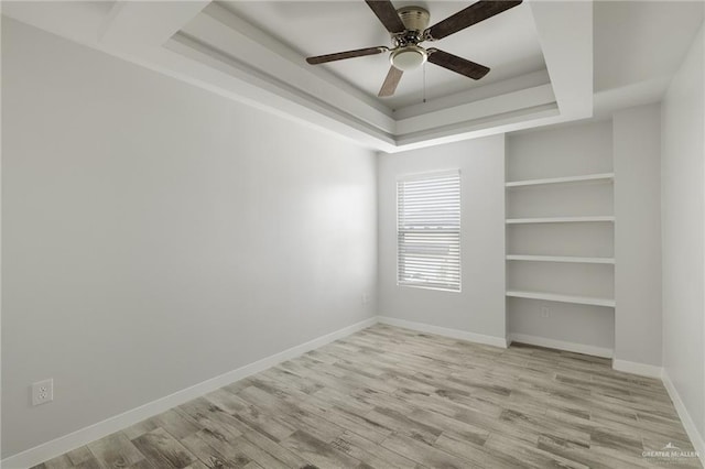 spare room with light hardwood / wood-style floors, a raised ceiling, and ceiling fan