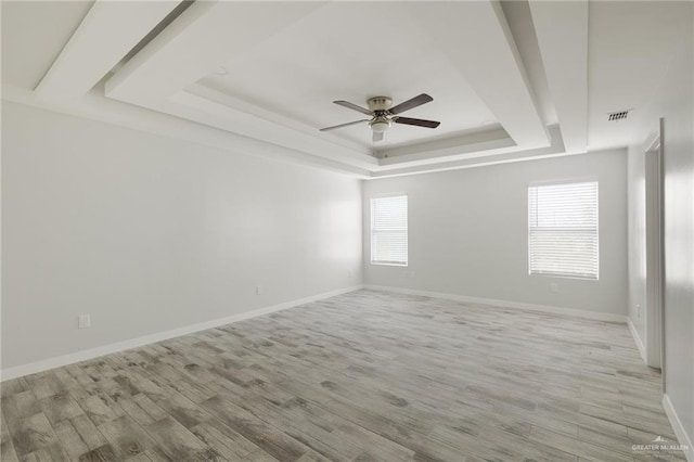 empty room with ceiling fan, a raised ceiling, and light wood-type flooring