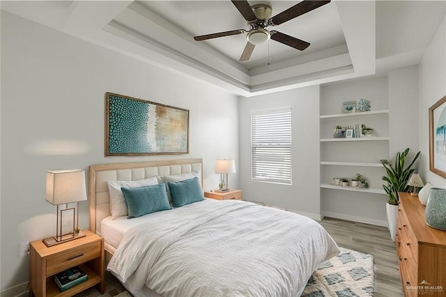 bedroom with ceiling fan, a tray ceiling, and light hardwood / wood-style floors