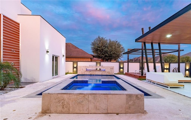 pool at dusk with an in ground hot tub and a patio area