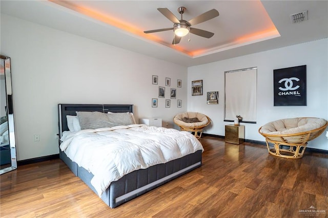 bedroom featuring ceiling fan, wood-type flooring, and a tray ceiling