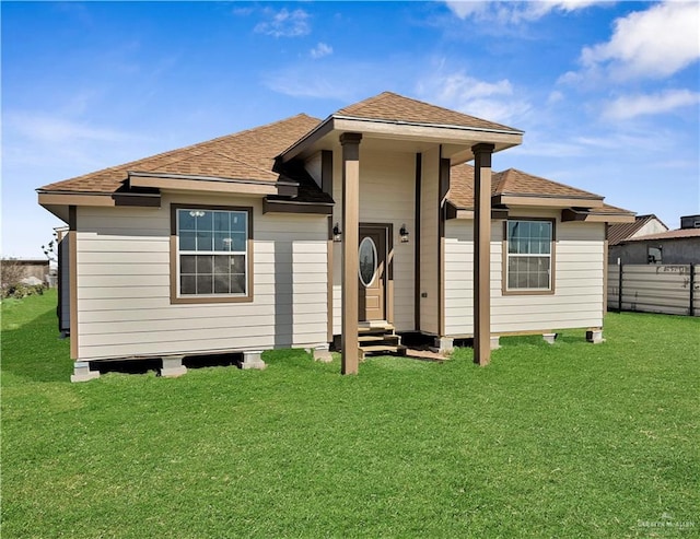 rear view of property featuring entry steps, a lawn, fence, and roof with shingles