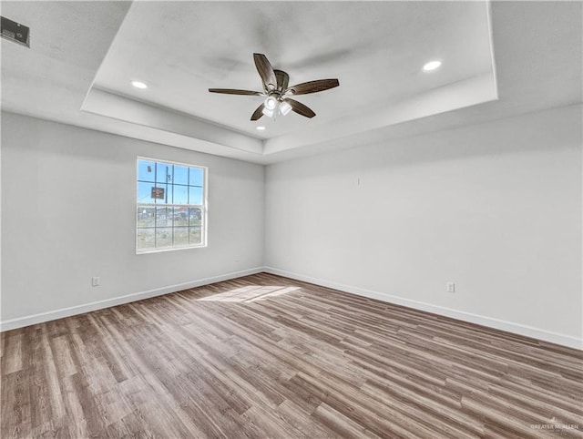 unfurnished room with recessed lighting, a tray ceiling, baseboards, and wood finished floors