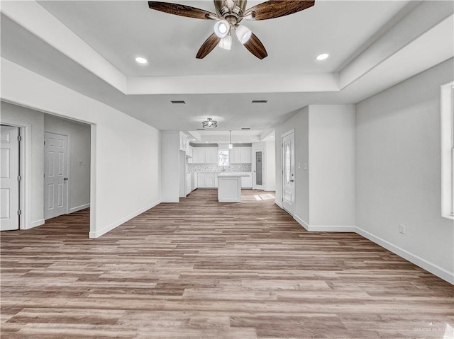 unfurnished living room with light wood-style flooring, baseboards, and a tray ceiling