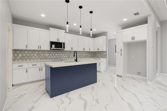 kitchen with pendant lighting, white cabinetry, sink, and a kitchen island with sink